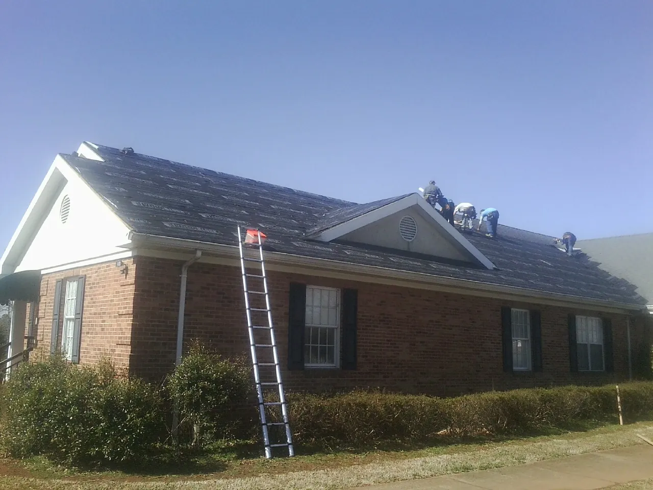Crew tearing shingles off a brick ranch roof with a ladder set — Emergency Roof Repair work by our crew in Boswell