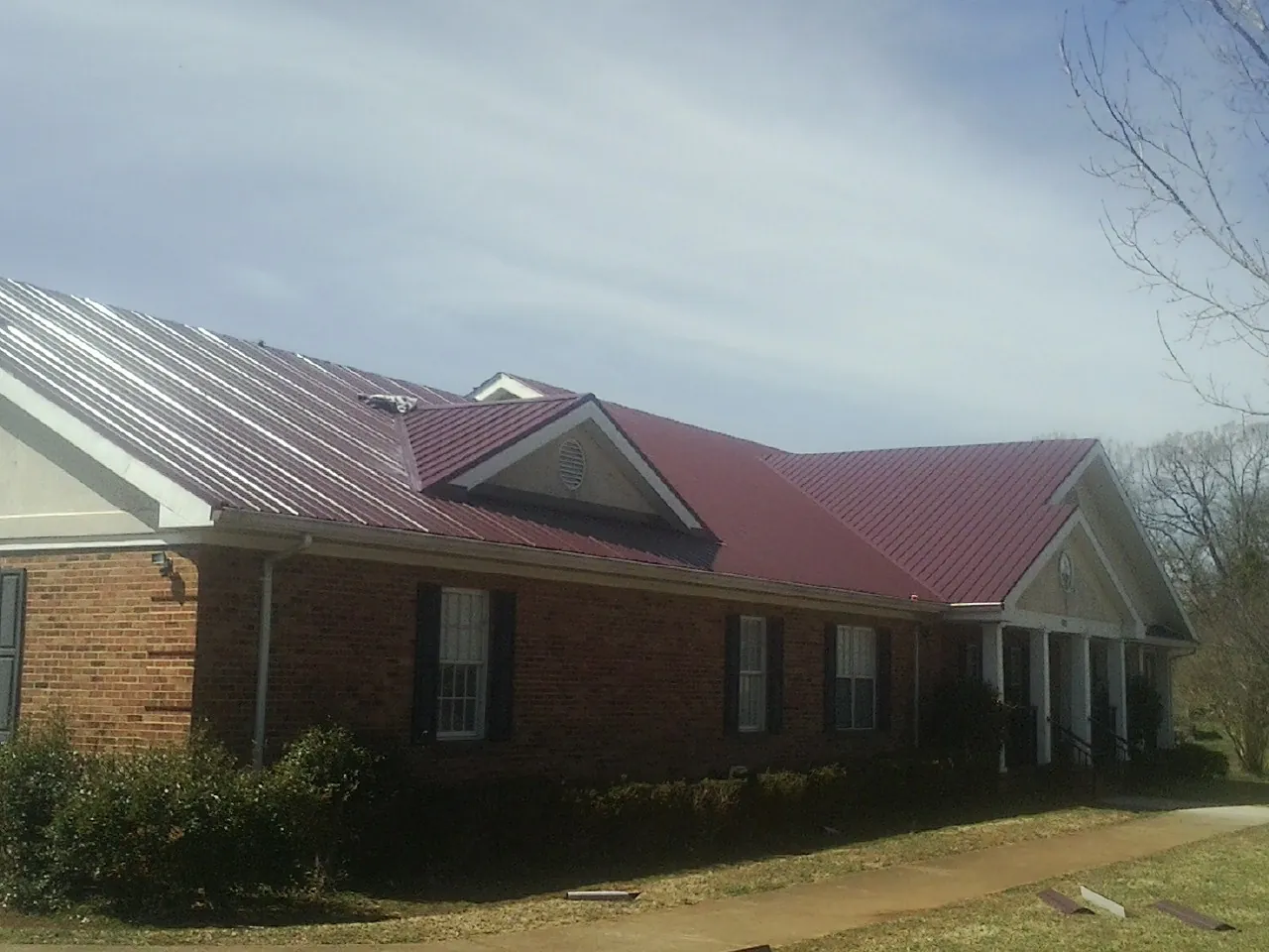 Red metal roof with gabled entries on a long brick building, from a Hail Damage Roof Repair job in Boswell