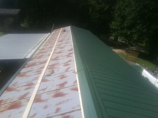 Old rusted panels beside newly installed green metal roofing — Wind Damage Roof Repair by Roofing Brothers in Boswell