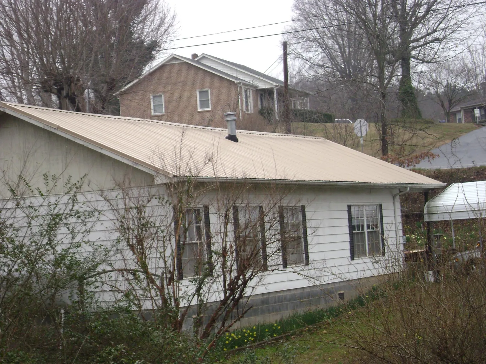 Tan metal roof on a white sided house set into a hillside — Commercial Roofing by Roofing Brothers in Boswell